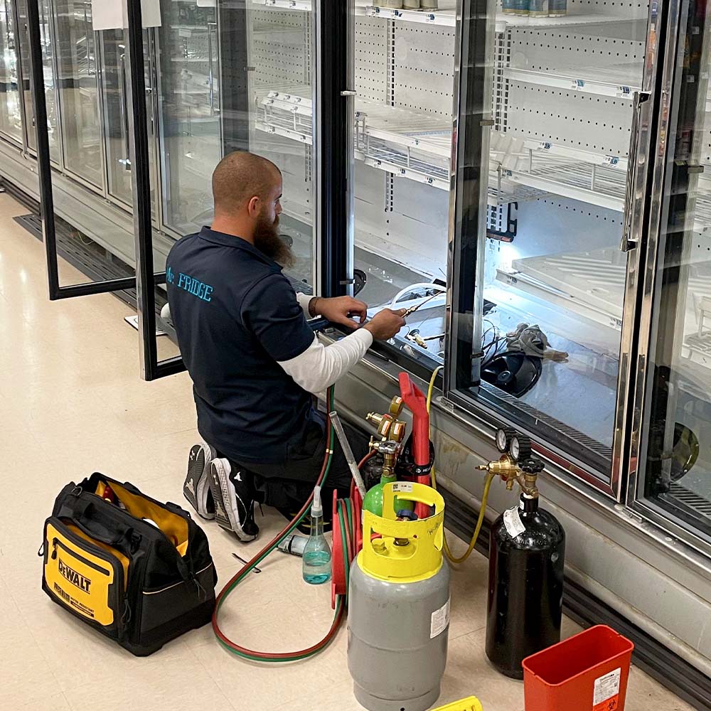 Mr. Fridge technician recharging Freon on a display cooler, providing dependable commercial fridge repair services.